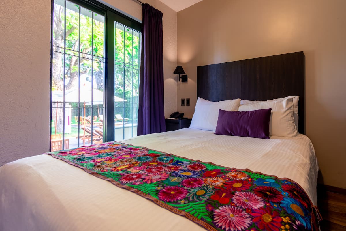 A hotel room with a large bed, a nightstand, a lamp, and a window with curtains.