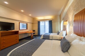 A hotel room with two beds, a desk, a television, and a window with curtains.