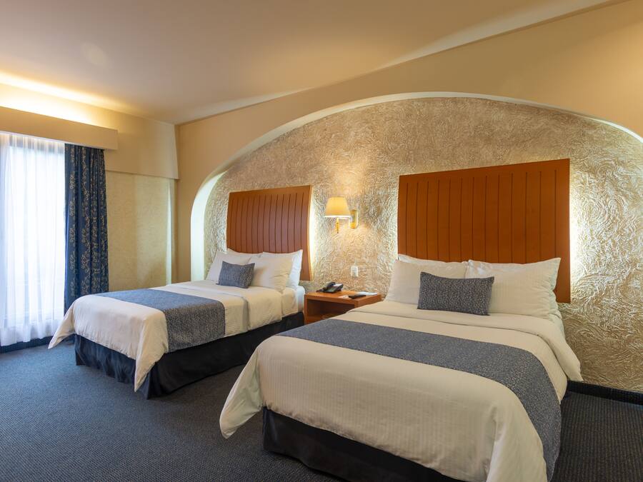 Habitación de hotel con dos camas, una pared curva y un ventanal con cortinas.