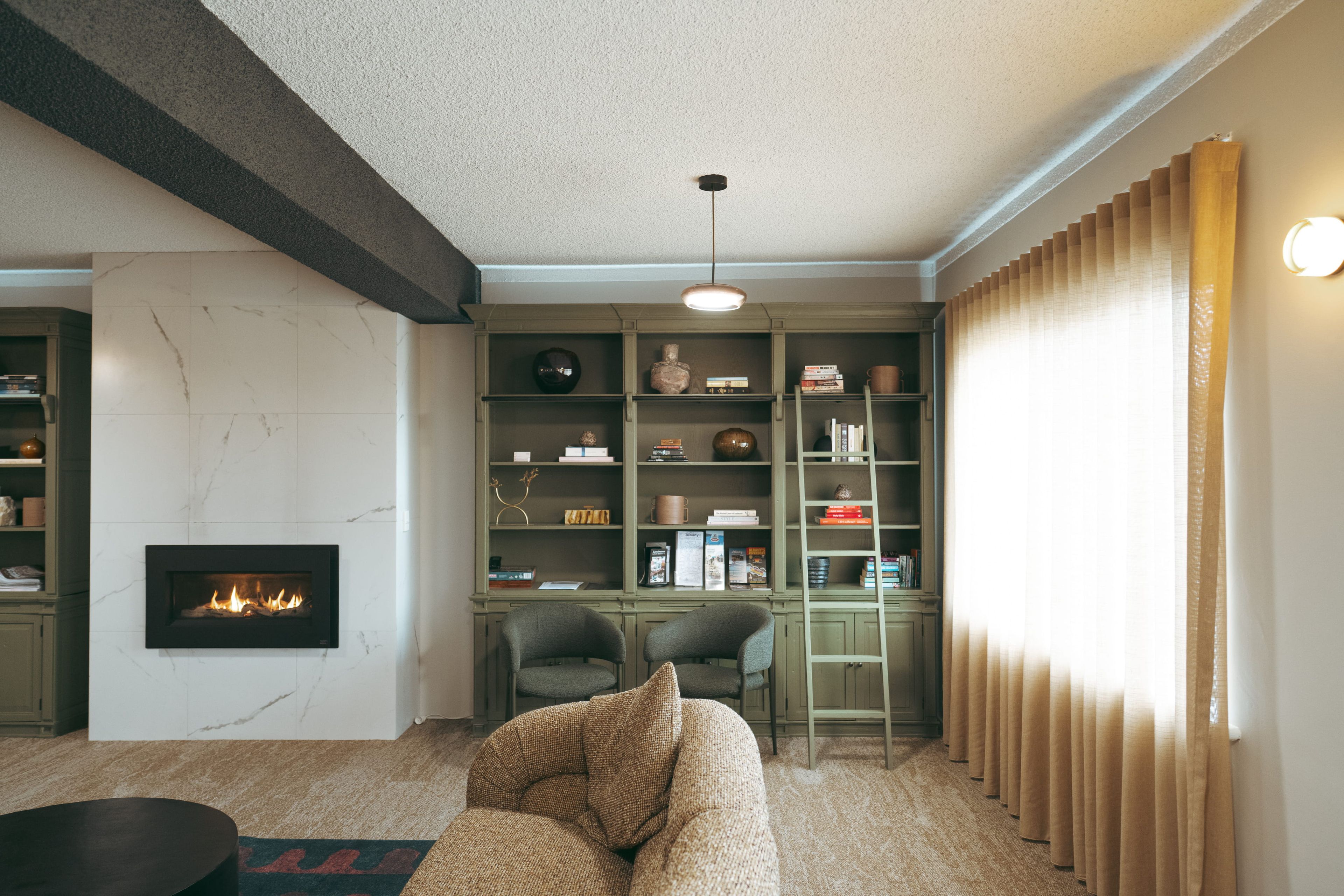 A living room with a fireplace, bookshelves, a sofa, and a window with curtains.