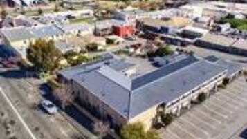 An aerial view of a commercial area with a large building, parking lots, and a road leading to the sea.