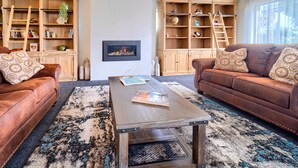 A living room with two brown leather sofas, a wooden coffee table, and built-in wooden shelving units with books and decorative items. - Albany Motel & Apartments (Albany)