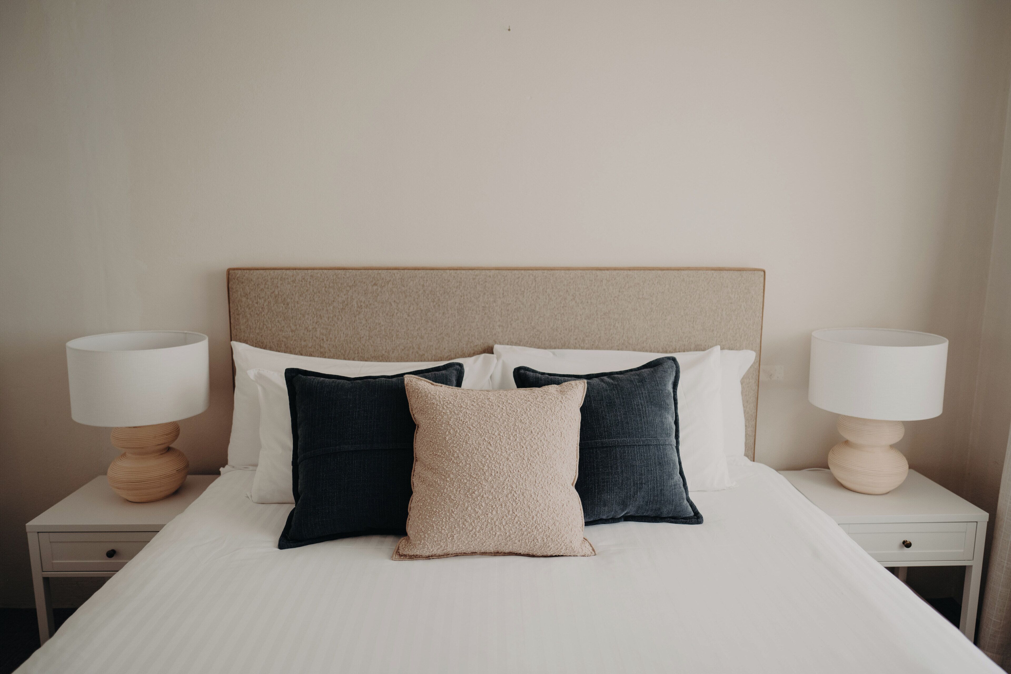 A neatly made bed with a headboard, two bedside tables with lamps, and a drawer.