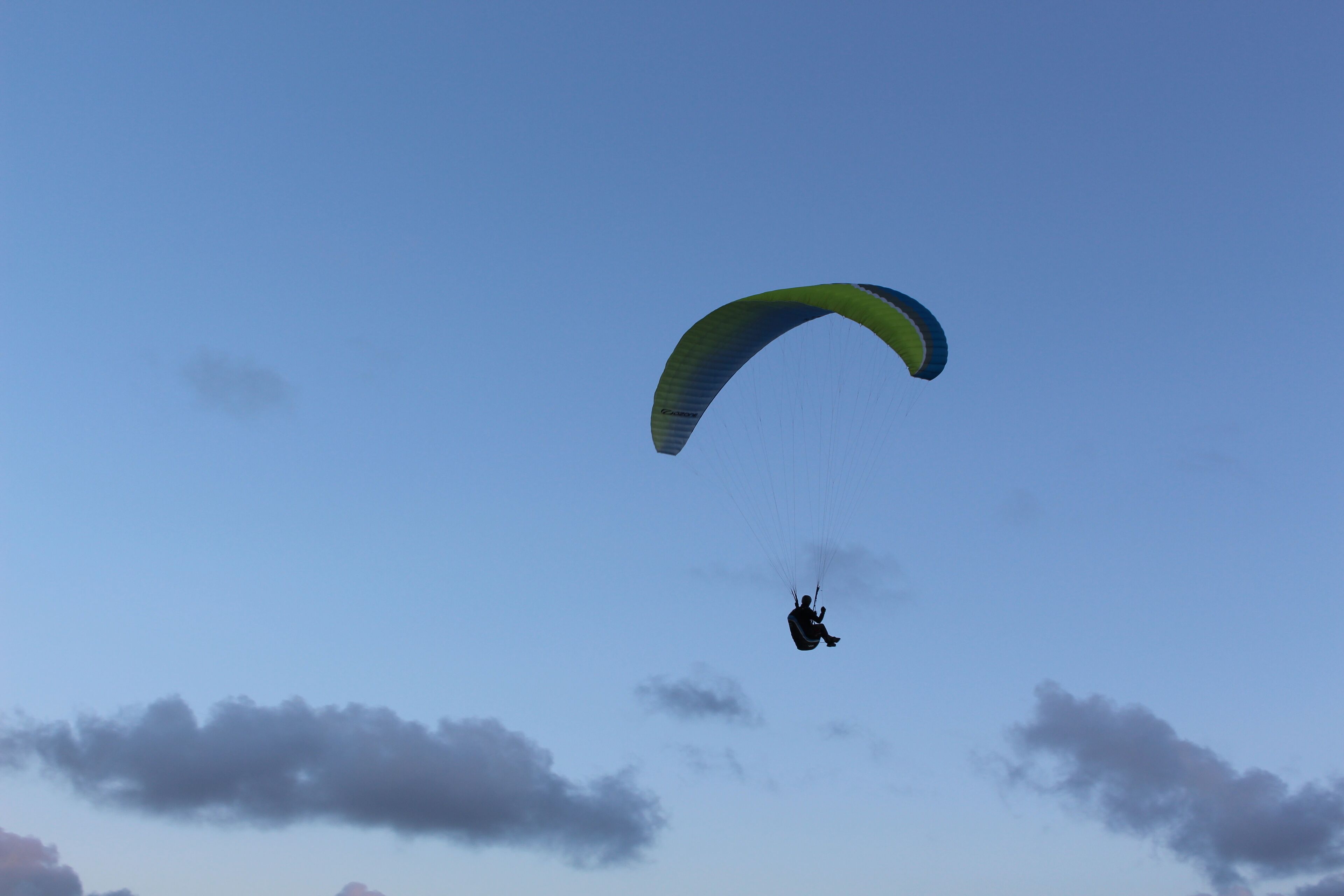 Una persona practicando paratrike con un paracaídas verde y azul, bajo un cielo despejado.