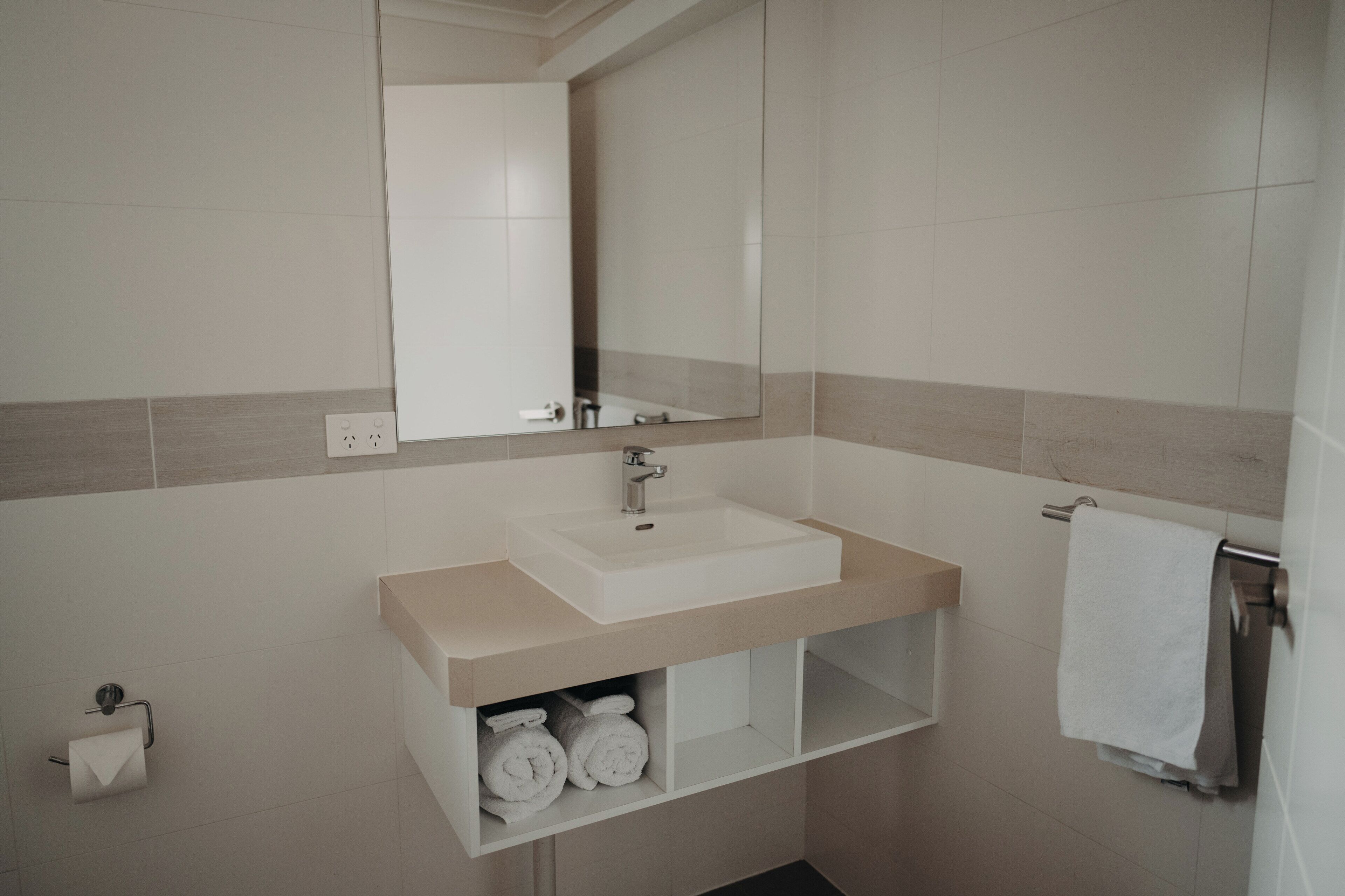 A bathroom with a sink, mirror, towel rack, and toilet paper holder.