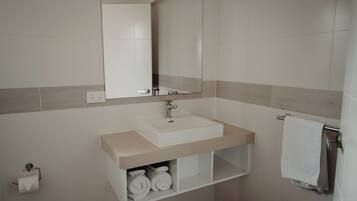 A bathroom with a sink, mirror, towel rack, and toilet paper holder.