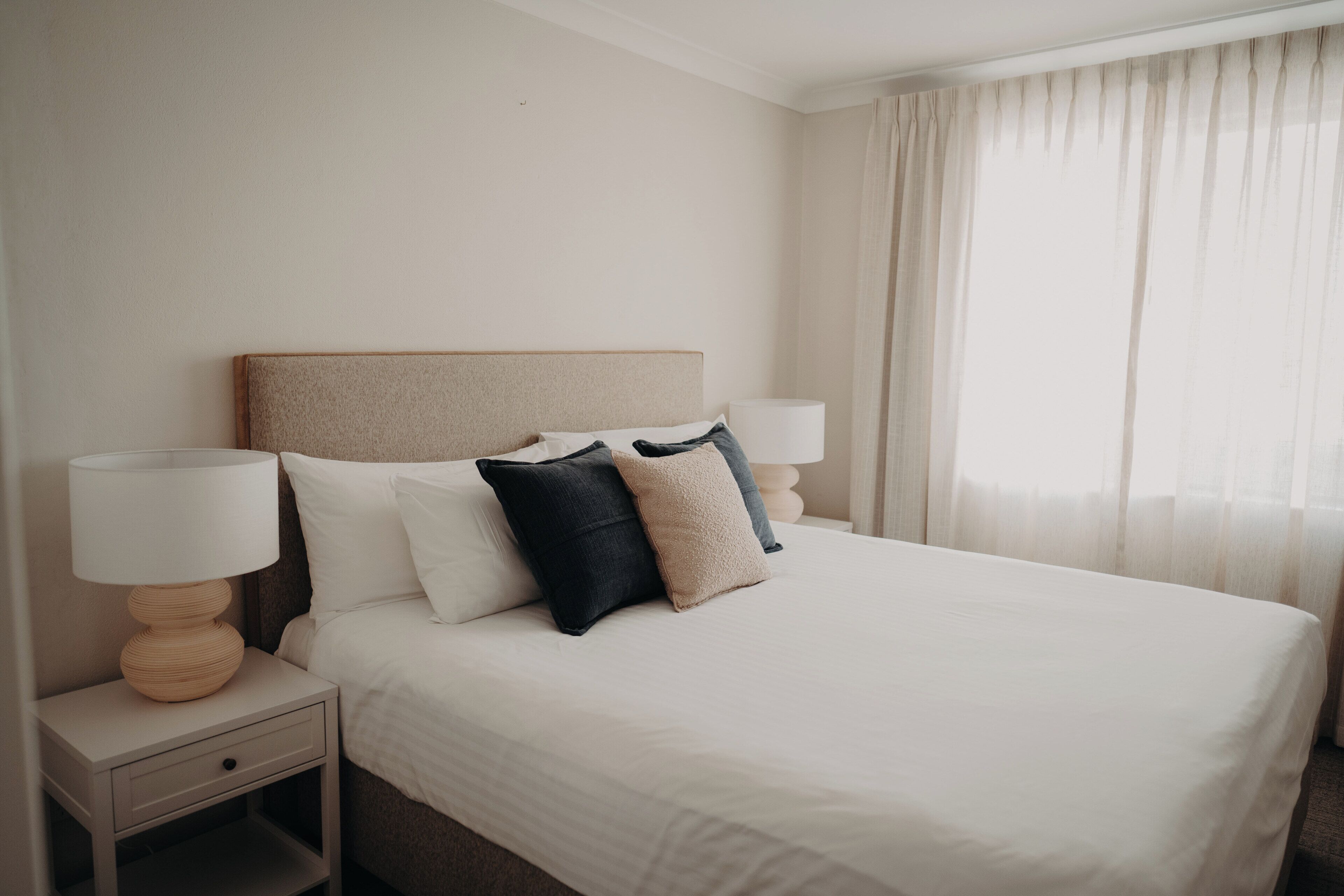 A hotel room with a bed, two bedside tables, a lamp, and a window with curtains.