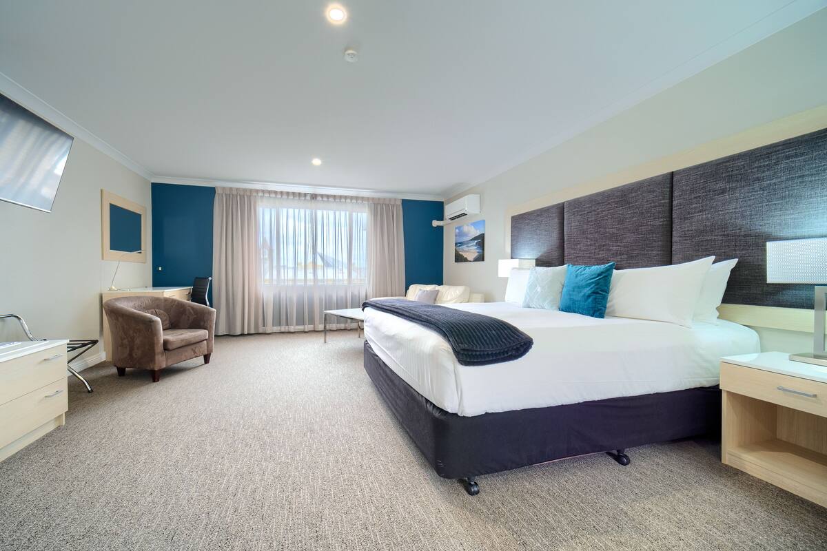 Ein Hotelzimmer mit einem großen Bett, einem Schreibtisch, einem Stuhl und einem Fenster mit Vorhängen.