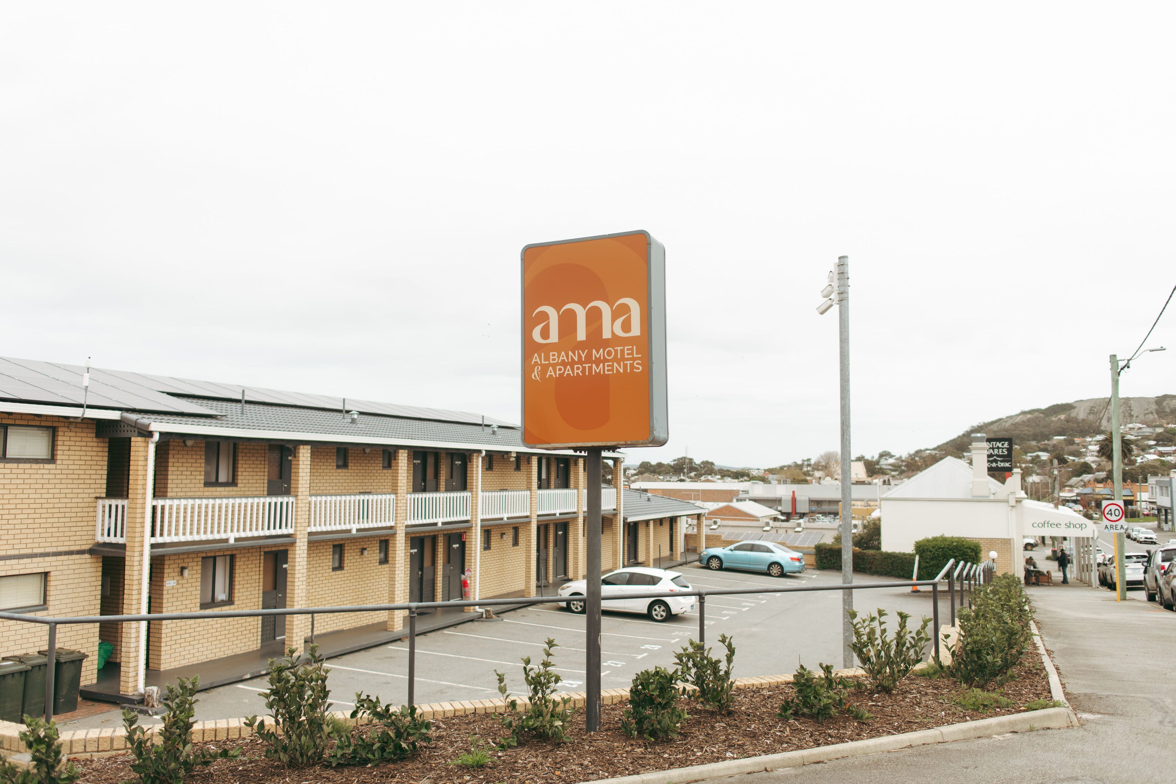 Um motel com uma placa visível, estacionamento e vista da rua com edifícios e carros.