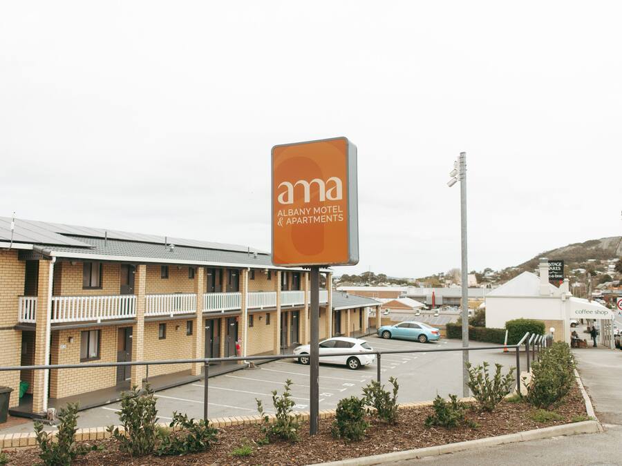 Un motel avec une enseigne bien visible, un parking et une vue sur la rue, avec des bâtiments et des voitures.