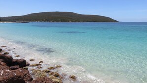 A beach with clear turquoise water, rocky shoreline, and a distant green hill. - Albany Motel & Apartments (Albany)