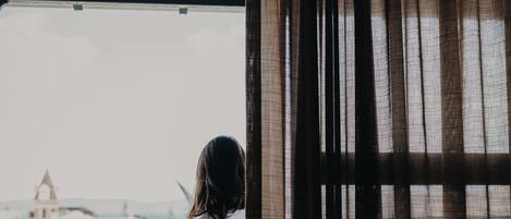 A person sitting on a chair by a window with a view of a building and a balcony.