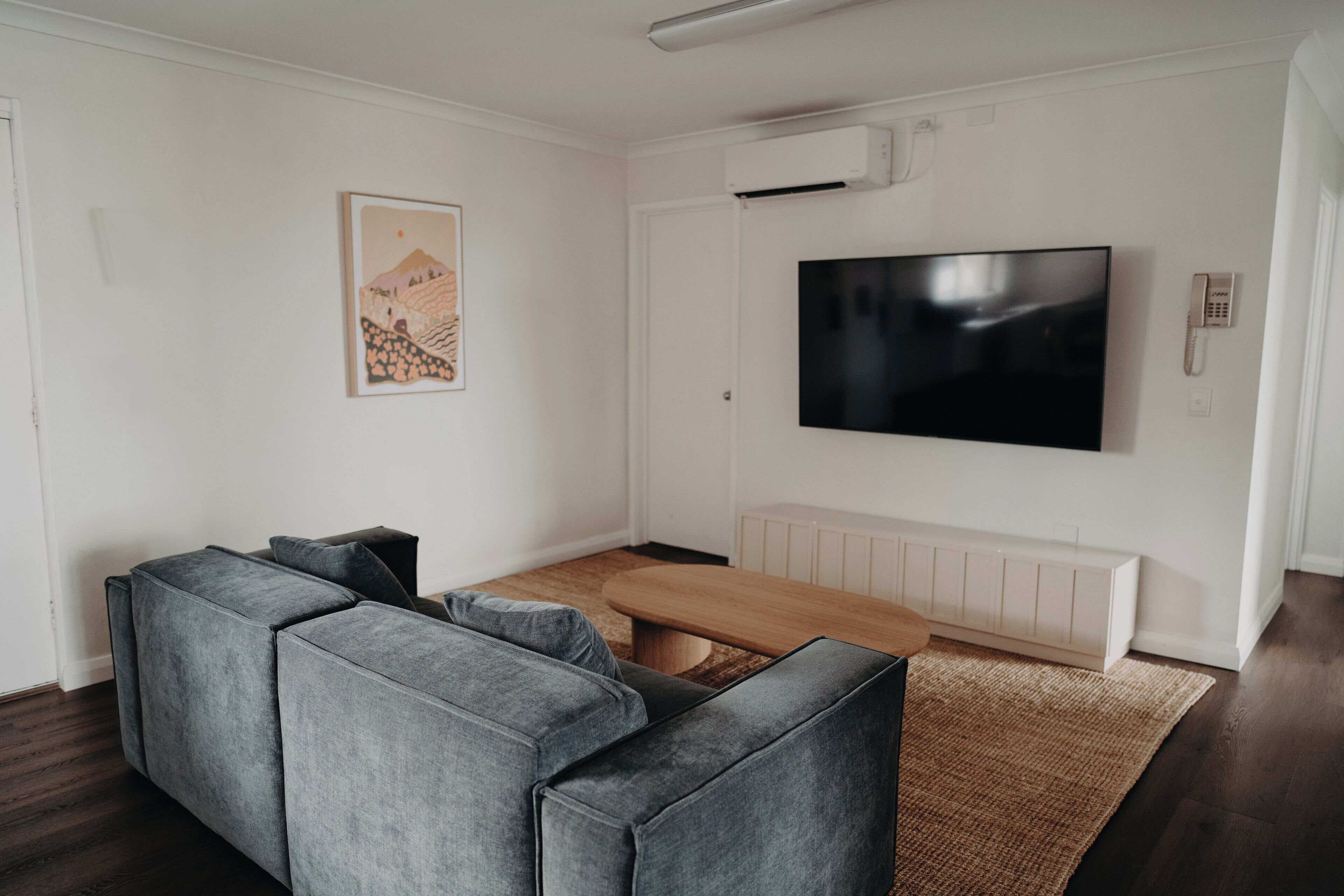 Una sala de estar moderna con un sofá seccional, una mesa de centro de madera, un televisor de pantalla plana montado en la pared y un radiador abajo.