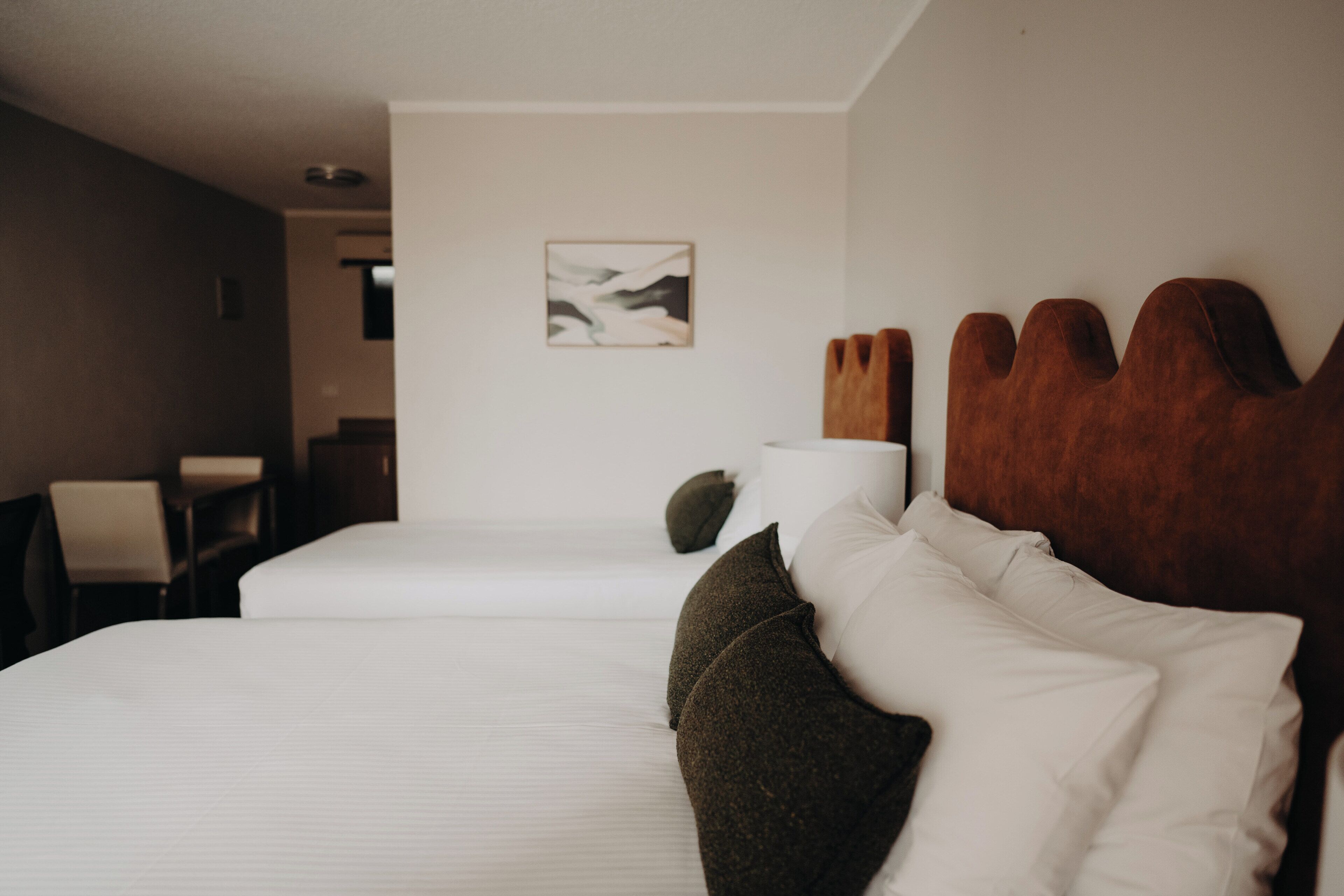 Habitación de hotel con dos camas, cabecero de madera, un cuadro en la pared y una silla.