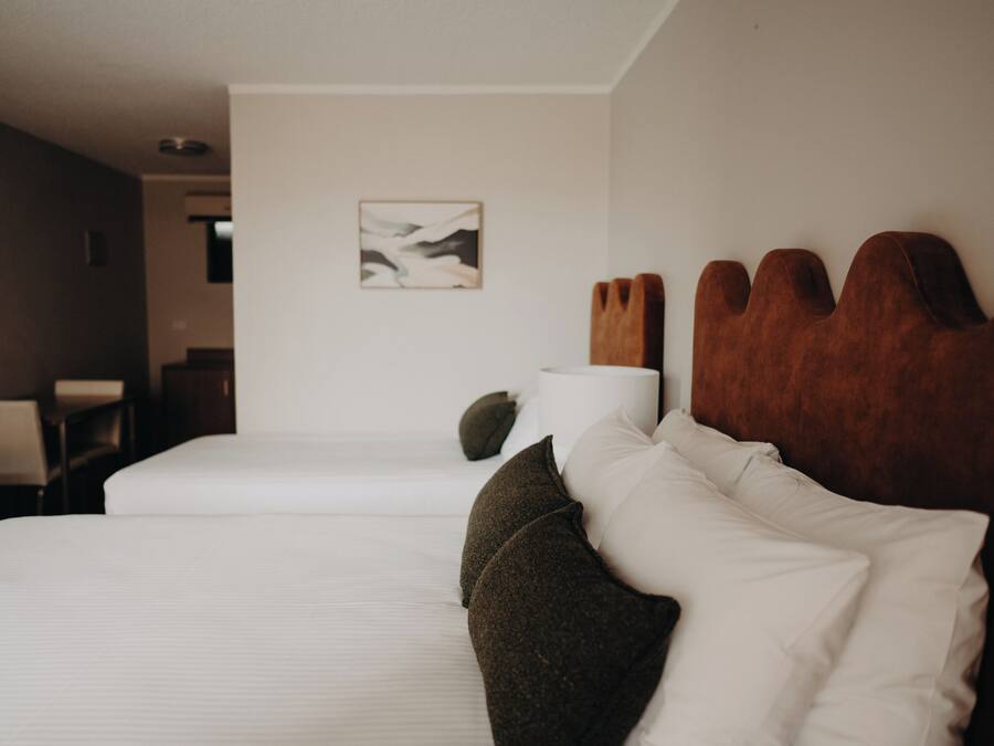 Habitación de hotel con dos camas, cabecero de madera, un cuadro en la pared y una silla.