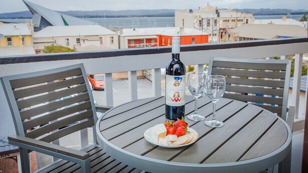 A balcony with a table set for two, featuring a bottle of wine, a glass, and a plate of cheese and strawberries. - Albany Motel & Apartments (Albany)