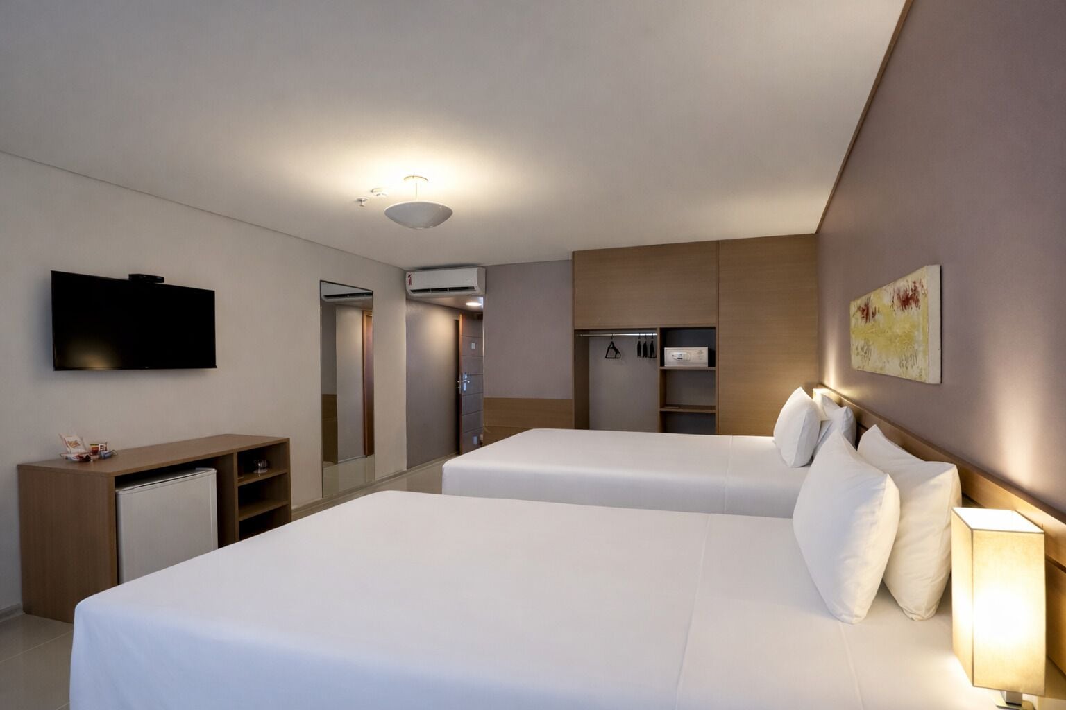 Habitación de hotel con dos camas, televisión, escritorio, armario y espejo.