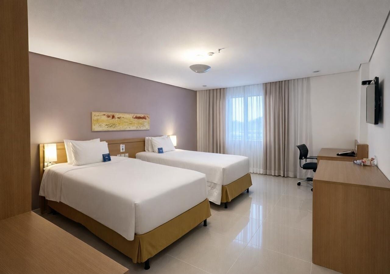 A hotel room with two beds, a desk, a chair, and a TV on the wall.