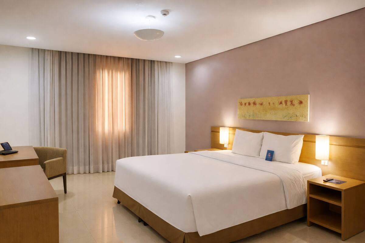 Habitación de hotel con una cama grande, un escritorio, una silla y una mesita de noche.