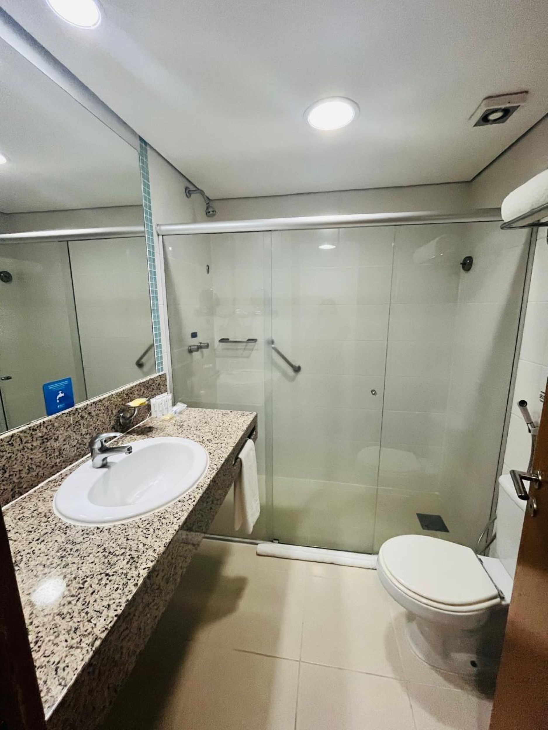 A bathroom with a granite countertop sink, a glass shower enclosure, and a white toilet.