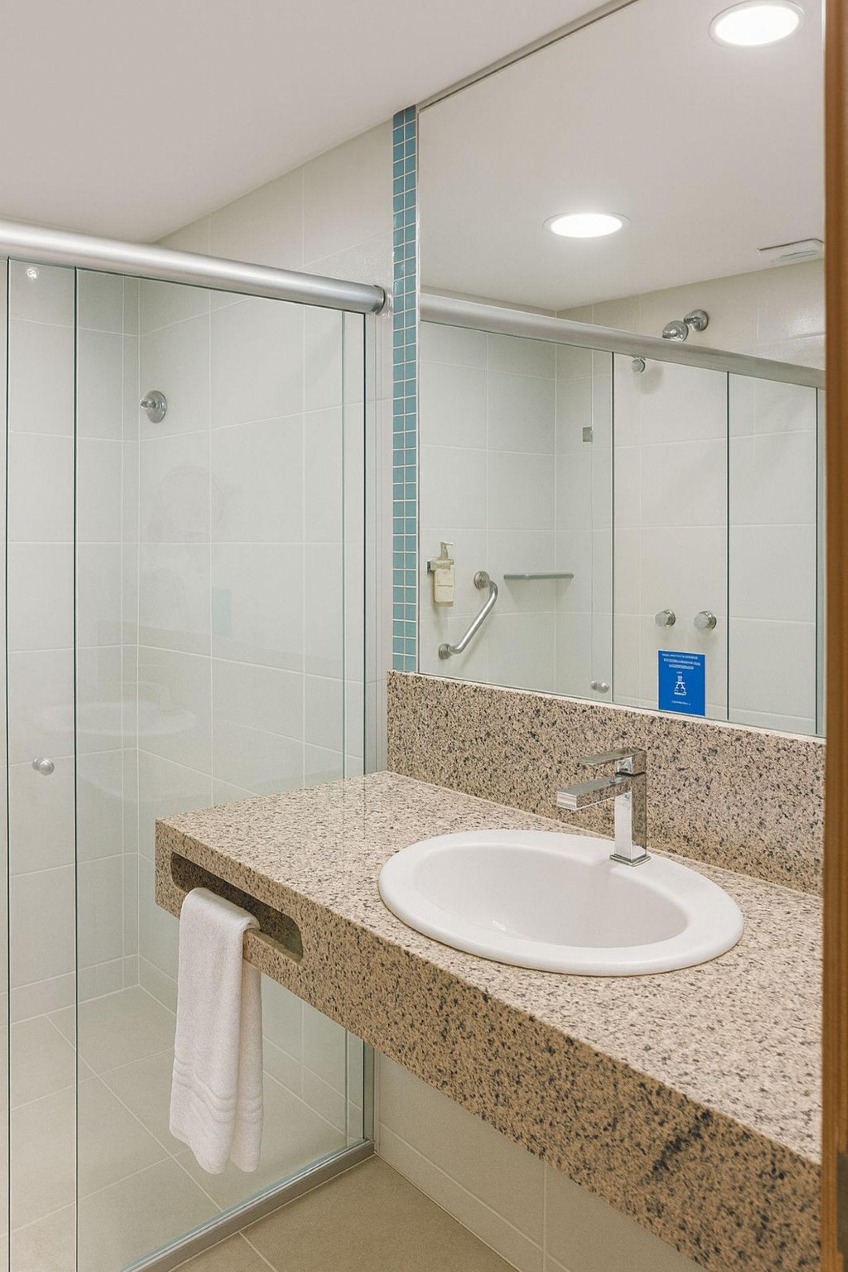 A modern bathroom with a glass shower enclosure, a granite countertop sink, and a mirror with a blue sign.