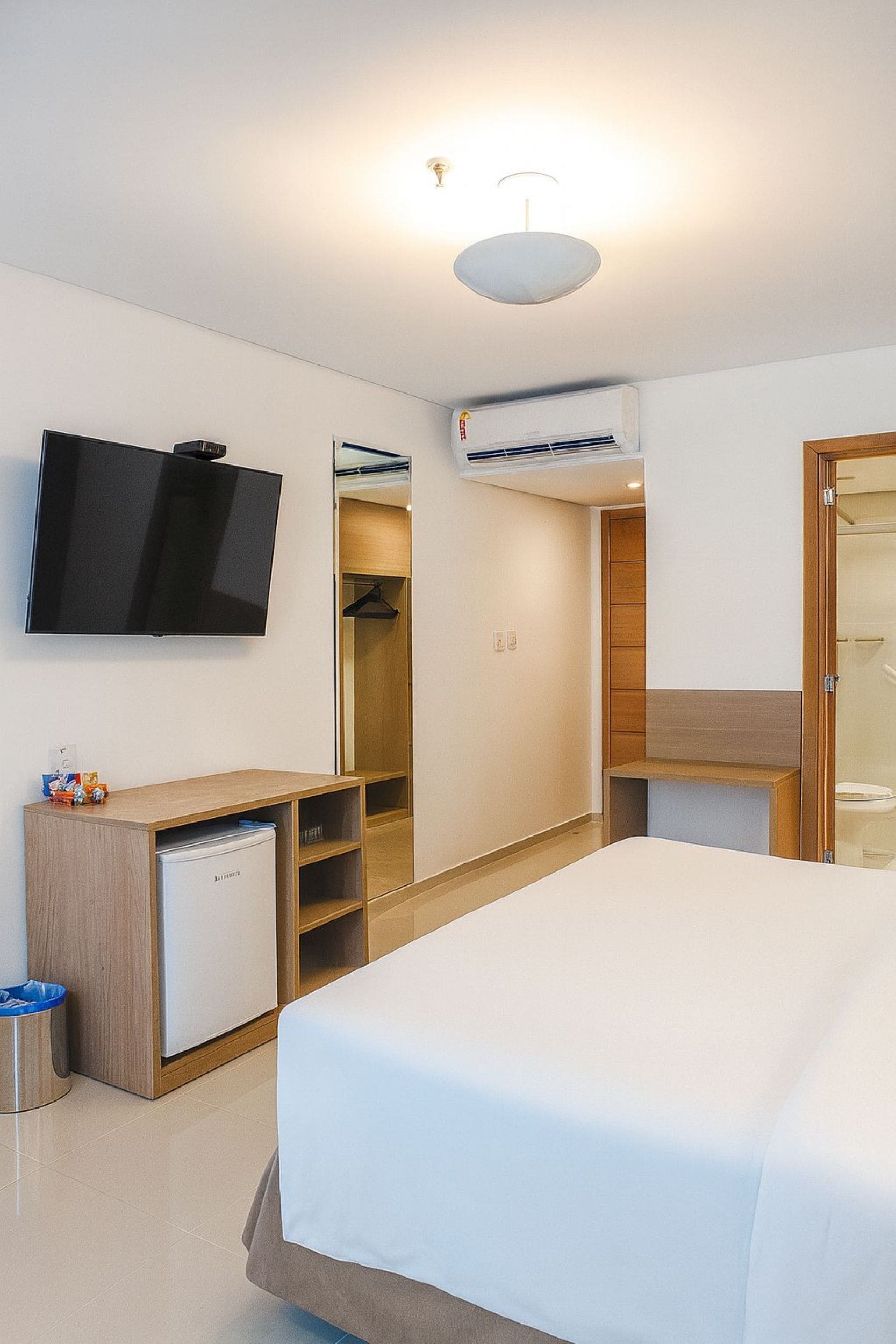 A hotel room with a bed, a TV, a wardrobe, a desk, and an air conditioning unit.