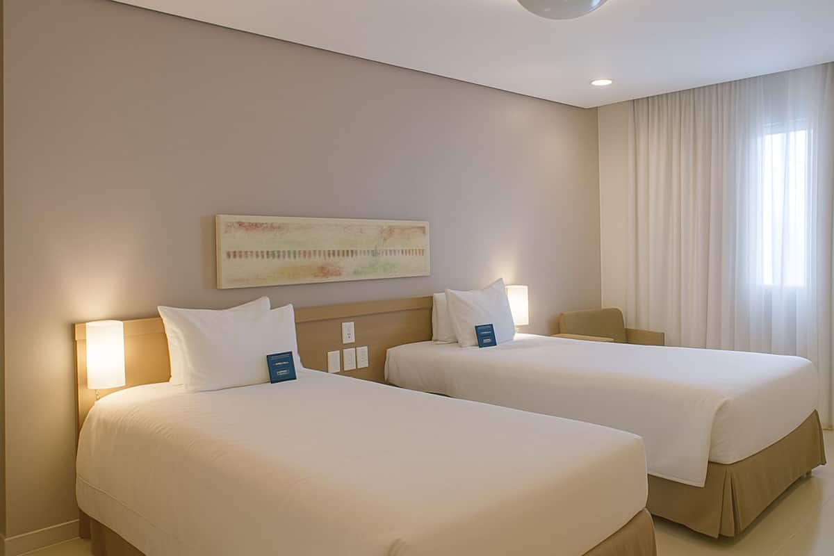 Habitación de hotel con dos camas, un ventanal con cortinas y un cuadro en la pared.