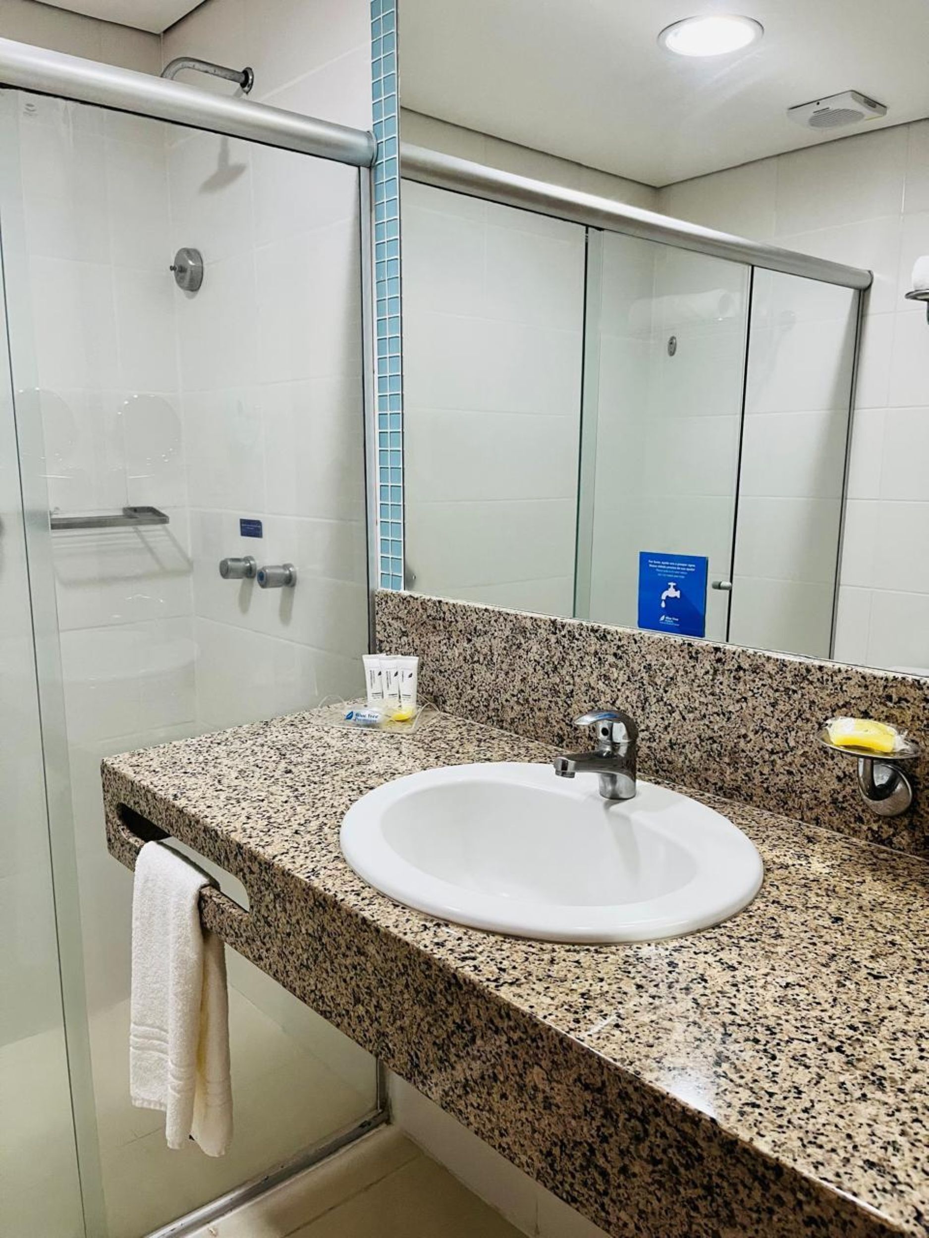 A bathroom with a granite countertop, a white sink, a mirror, and a glass shower enclosure.