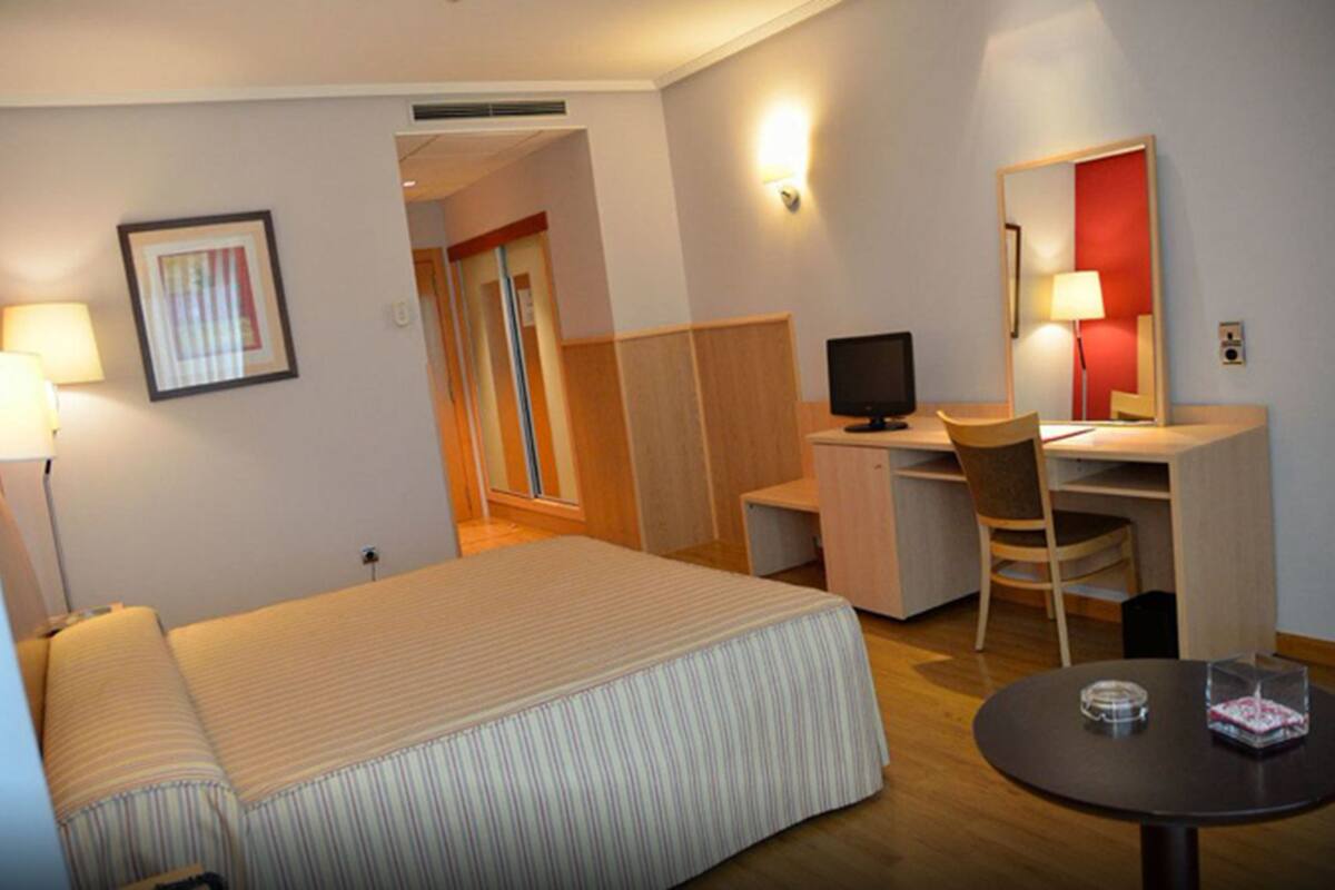 A hotel room with a bed, desk, chair, and a small table.