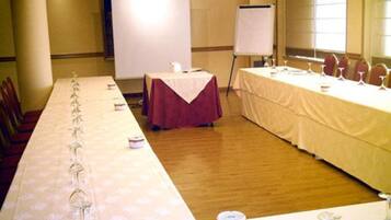 Un salón de conferencias con una larga mesa dispuesta para una reunión, una pizarra y un rotafolio.