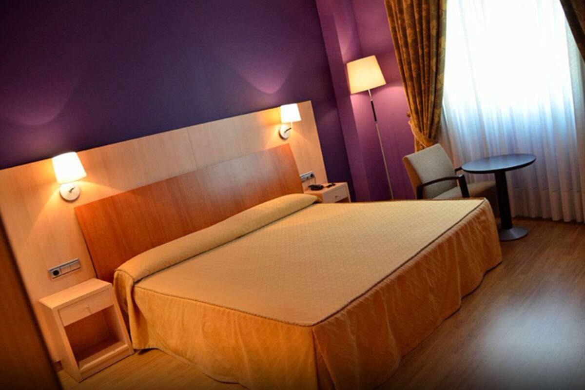 A hotel room with a large bed, bedside tables, a chair, and a small table.