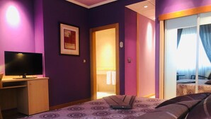 A hotel room with a bed, a desk with a TV, a door leading to a bathroom, and a window with curtains. - Hotel Villa de Benavente (Benavente)