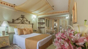 A hotel room with a large bed, a nightstand with a lamp, a mirror, and a small table with a chair. - Hotel Villa Las Margaritas Plaza Cristal (Xalapa)