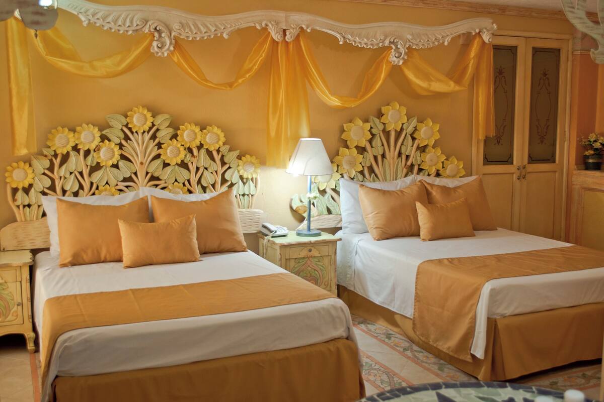 Ein Hotelzimmer mit zwei Betten, einem Nachttisch mit Lampe und einer Wand mit Sonnenblumen-Dekoration.