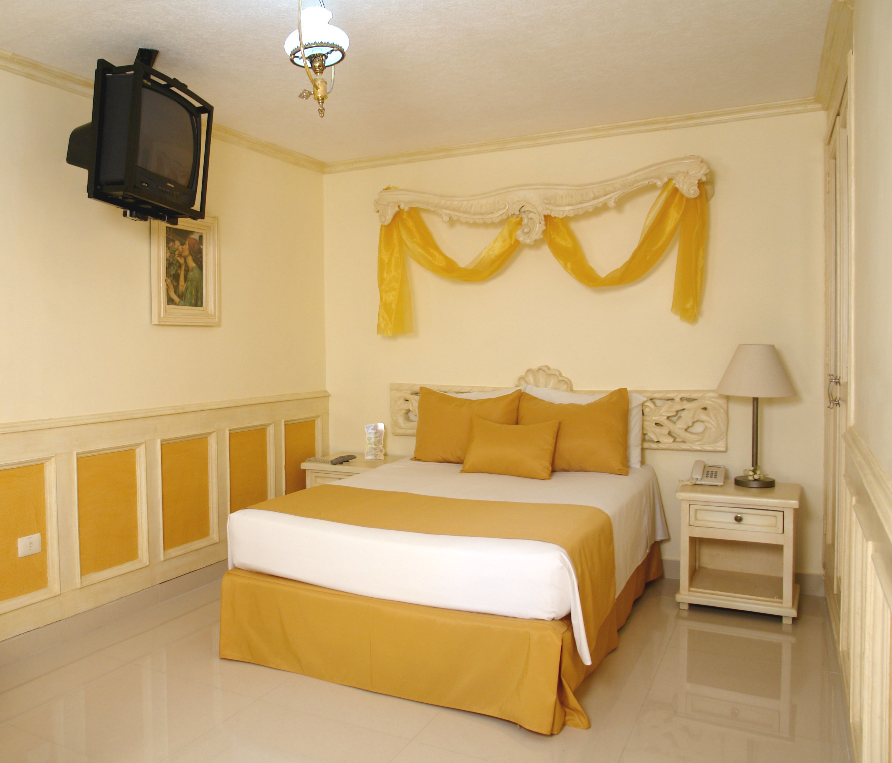 Une chambre d’hôtel équipée d’un lit, d’une table de chevet, d’une lampe et d’un téléviseur fixé au mur.