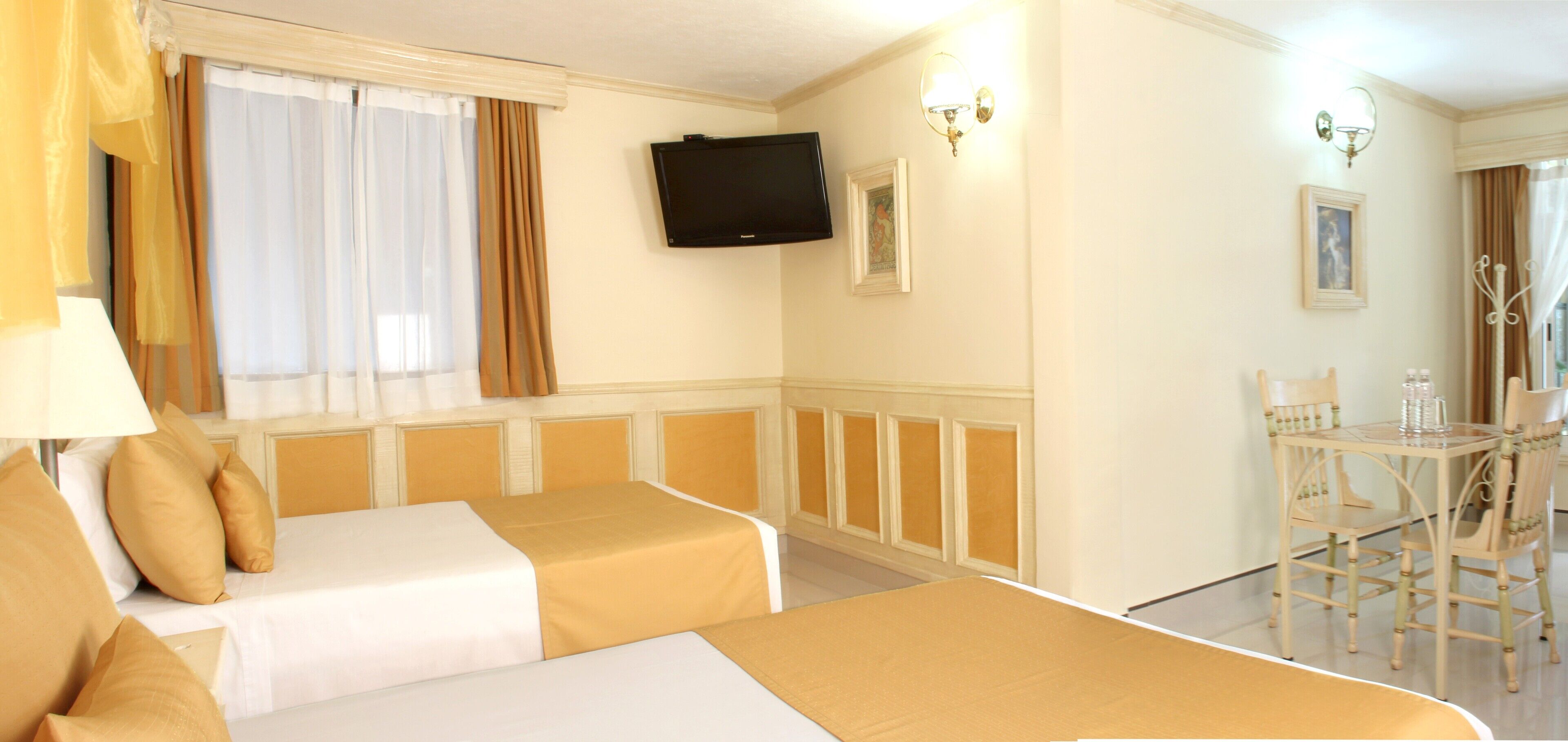 A hotel room with two beds, a TV, a dining area with a table and chairs, and a window with curtains.