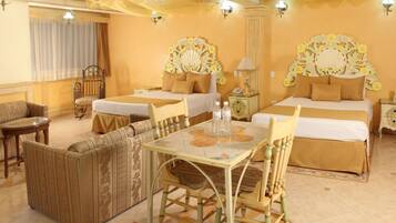 A hotel room with two beds, a sofa, a dining table, and a small side table.