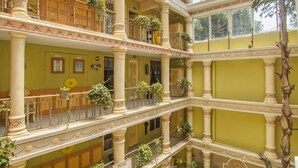 A multi-level atrium with green tables and chairs, potted plants, and a large tree. - Hotel Villa Las Margaritas Plaza Cristal (Xalapa)