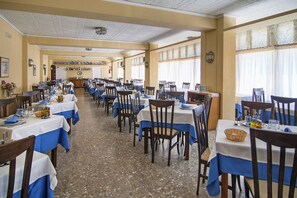 Ein geräumiger Speisesaal mit mehreren Tischen und Stühlen, die in Reihen angeordnet sind.