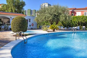 A swimming pool with a tiled deck, surrounded by greenery and a building with a red roof. - Hotel Vista Alegre (Benicassim)