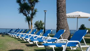 Una fila de sillones reclinables azules y blancos alineados en un césped, con una palmera y un farol.