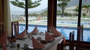 Una mesa de comedor preparada con servilletas rosas, platos y vasos, con vistas a una zona de piscina con sillas de descanso y un flotador.