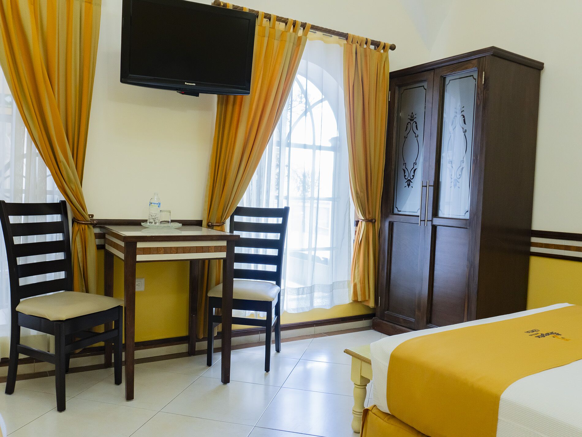 A hotel room with a bed, a desk with two chairs, a television, and a wardrobe.