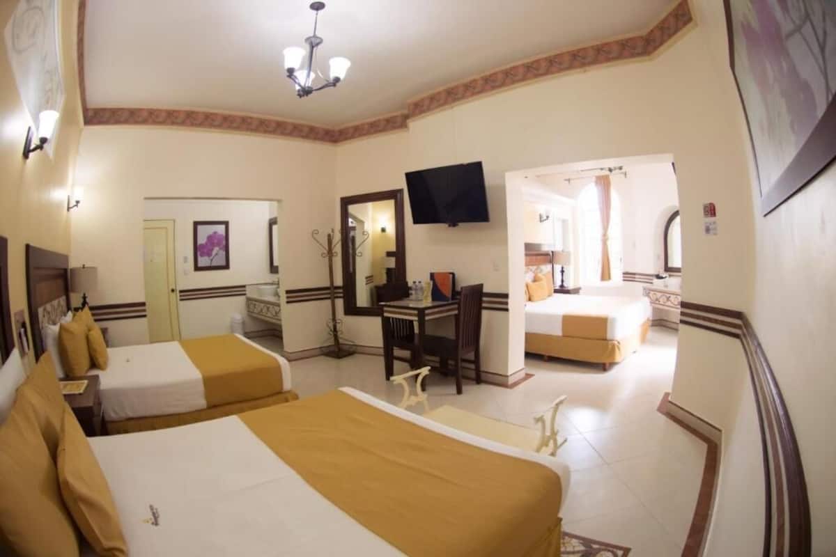 Une chambre d’hôtel avec deux lits, un bureau, une télévision et une salle de bain visible à travers une porte ouverte.