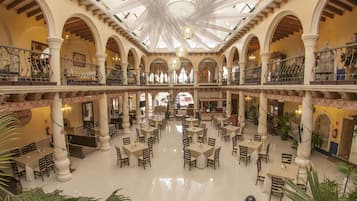A spacious, multi-level atrium with numerous tables and chairs, high ceilings, and ornate columns.