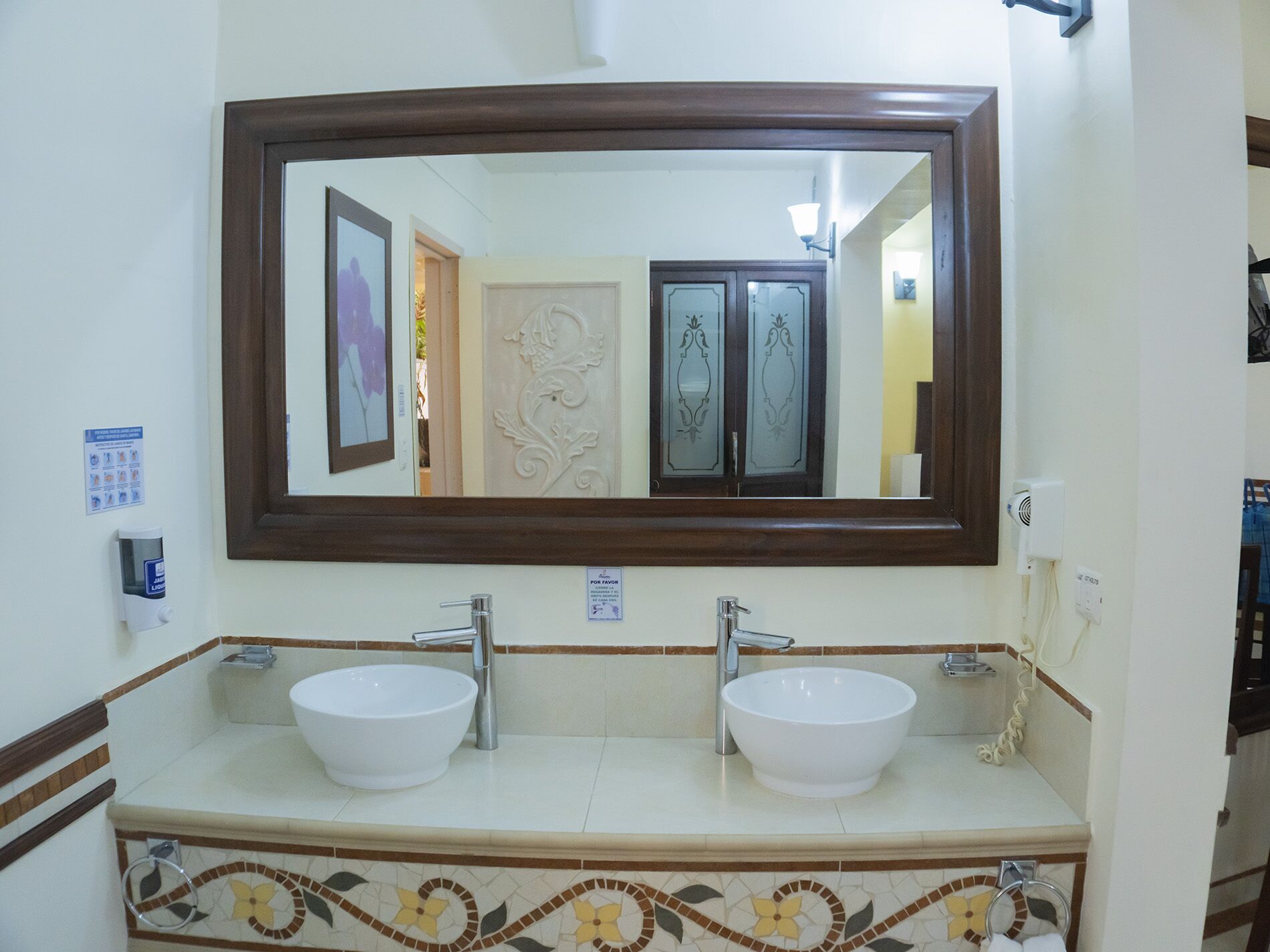 Casa de banho com duas pias, um espelho grande e uma moldura de azulejos decorativa.