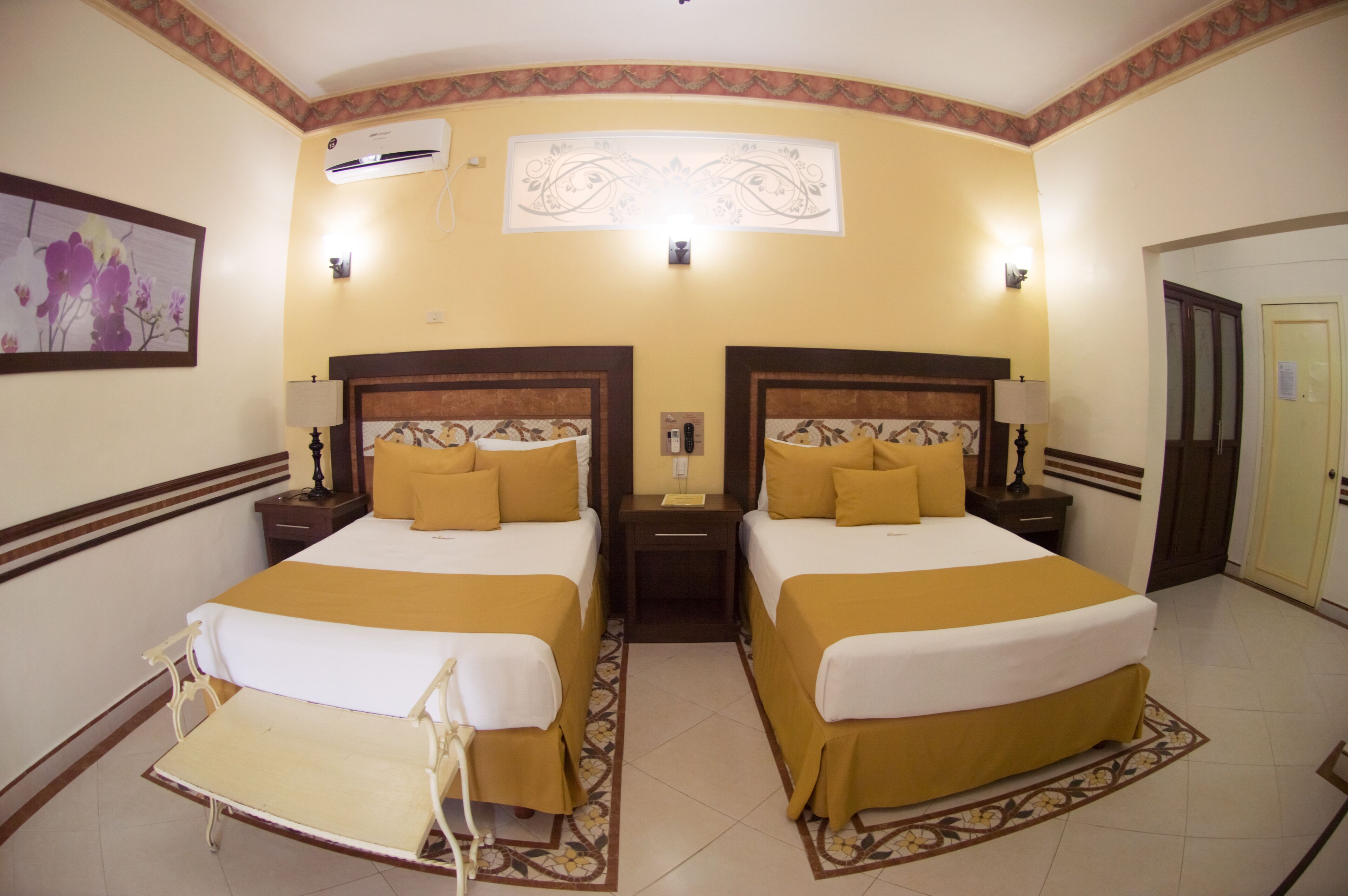 A hotel room with two beds, a chair, a nightstand, and a door.