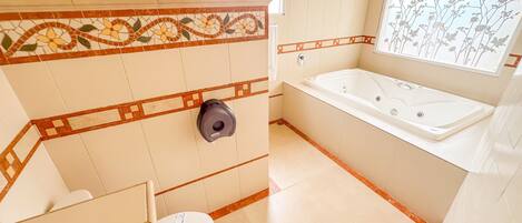 Un baño con inodoro, secamanos, bañera y ventana con vistas a un jardín floral.