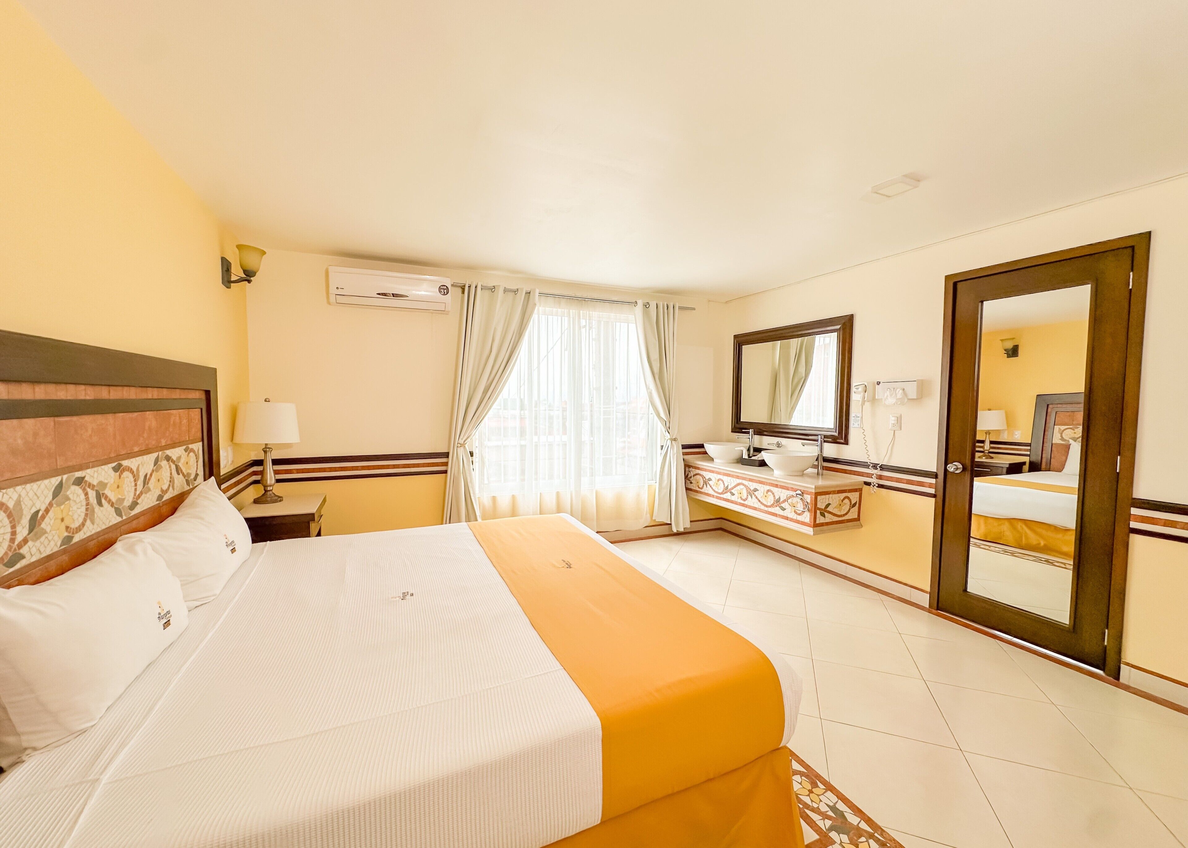 A hotel room with a bed, a bathroom with a mirror, and a view of the city.