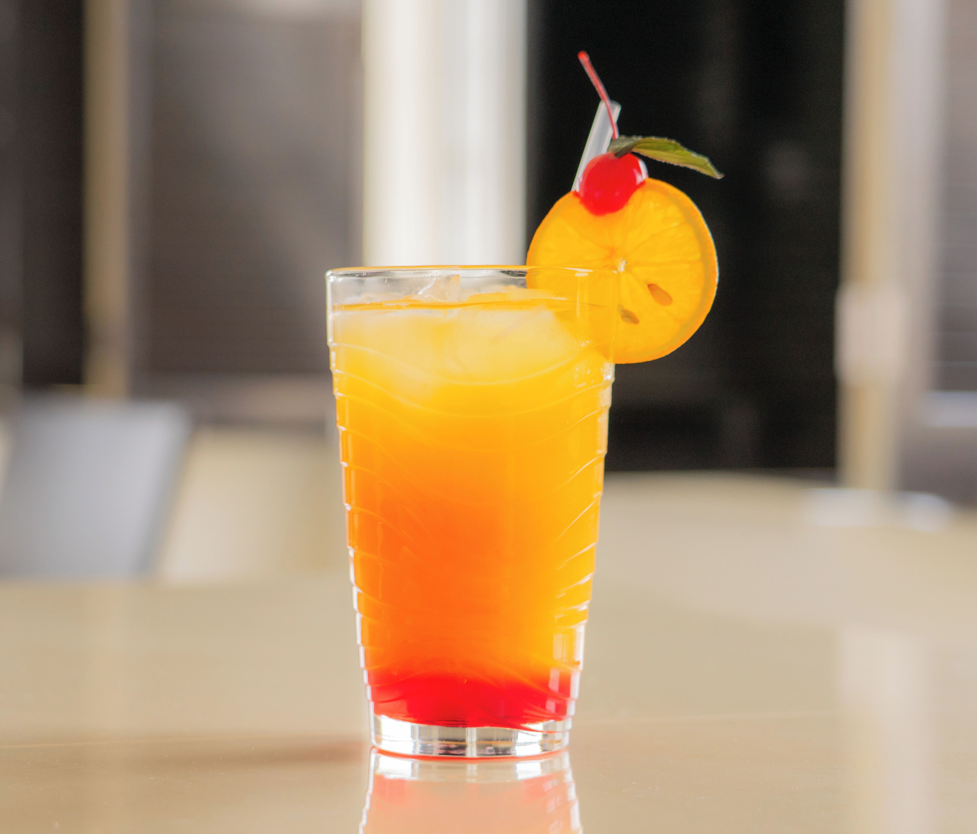 A tall glass with a gradient drink, a cherry, and a slice of orange on the rim.